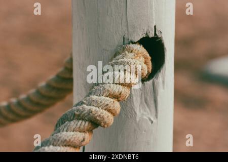 Weißes Seil aus Bio-Baumwolle auf einem weißen Holzzaun, Tor an einem Sandstrand. Hintergrund für Pfosten und Seile. Nautisches Sommerthema. Stockfoto