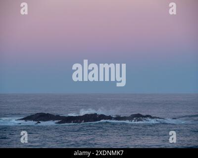 Wunderschöne Schichten von rosa und blauem Himmel Sonnenuntergang reflektiert in Wolken im Osten über dem Pazifik, Insel mit stürzenden Wellen, NSW Australien Stockfoto