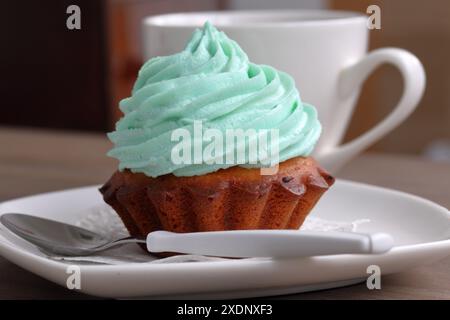 Creme Kuchen und eine Tasse Kaffee. Der Kuchen liegt auf einer Untertasse. In der Nähe eines Kaffeelöffels. Stockfoto