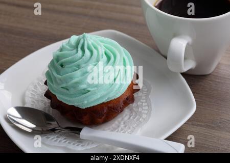 Creme Kuchen und eine Tasse Kaffee. Der Kuchen liegt auf einer Untertasse. In der Nähe eines Kaffeelöffels. Stockfoto