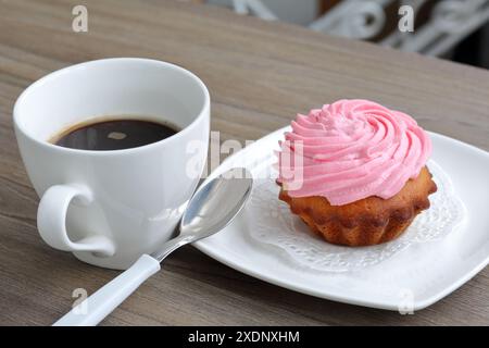 Creme Kuchen und eine Tasse Kaffee. Der Kuchen liegt auf einer Untertasse. In der Nähe eines Kaffeelöffels. Stockfoto
