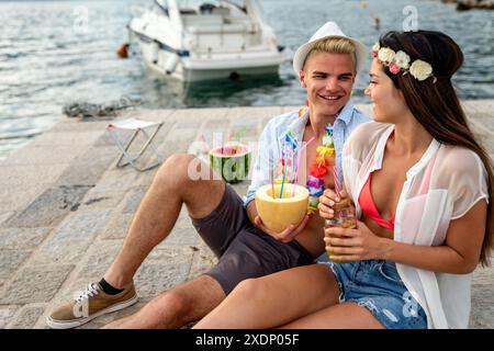 Glückliche, junge, verliebte Paare aus mehreren ethnischen Gruppen sind auf einem Date und genießen Cocktails am Strand Stockfoto