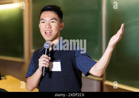 Ein junger Schüler im Teenageralter hält eine Präsentation, während er in das Mikrofon vor dem Klassenzimmer spricht Stockfoto
