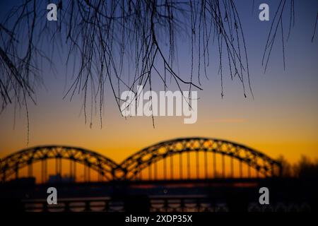 Eine wunderschöne Landschaft bei Sonnenaufgang mit eiserner Brücke über den gefrorenen Fluss Daugava in der lettischen Hauptstadt Riga. Winterlandschaft Nordeuropas. Stockfoto