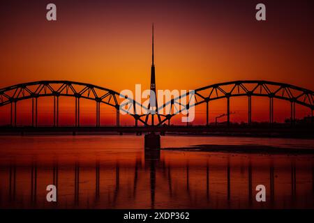 Eine wunderschöne Landschaft bei Sonnenaufgang mit eiserner Brücke über den gefrorenen Fluss Daugava in der lettischen Hauptstadt Riga. Winterlandschaft Nordeuropas. Stockfoto