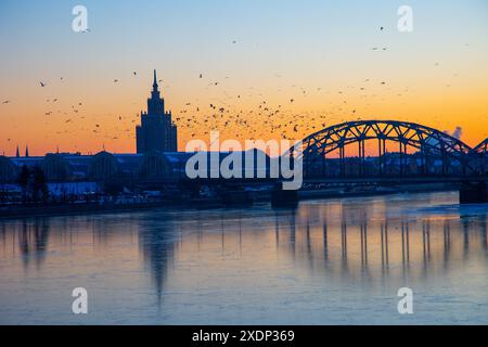 Eine wunderschöne Landschaft bei Sonnenaufgang mit eiserner Brücke über den gefrorenen Fluss Daugava in der lettischen Hauptstadt Riga. Winterlandschaft Nordeuropas. Stockfoto