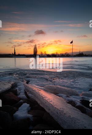 Eine wunderschöne Winterlandschaft bei Sonnenaufgang in der lettischen Hauptstadt Riga mit dem gefrorenen Fluss Daugava. Buntes Stadtbild Nordeuropas. Stockfoto