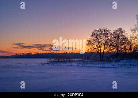 Eine wunderschöne Winterlandschaft mit gefrorenem See und Wald. Farbenfrohe Landschaft mit Morgenhimmel in Nordeuropa. Stockfoto