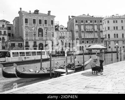 Venedig, Italien - 30. Juni 20220 zwei Gondoliere warten auf Touristen an einem Pier in venedig, mit Gondeln vertäut und historischen Gebäuden im Hintergrund Stockfoto