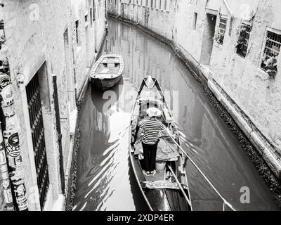 Venedig, Italien - 30. Juni 20220 Gondoliere mit gestreiftem Hemd und Hut auf einem schmalen Kanal in venedig, italien Stockfoto