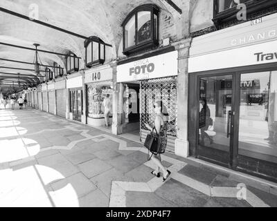 Venedig, Italien - 30. Juni 20220 Schwarzweiß-Foto einer Frau, die auf einem gemusterten Bürgersteig unter Bögen in venedig, italien, läuft, vorbei an geschlossenen Geschäften Stockfoto