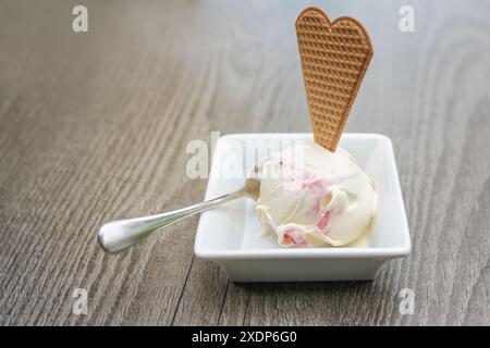 Ein Eislöffel mit Waffeln und Löffel in einer kleinen Schüssel auf einem grauen Holztisch, erfrischendes süßes Dessert, Kopierraum, ausgewählter Fokus, enge Ablage Stockfoto