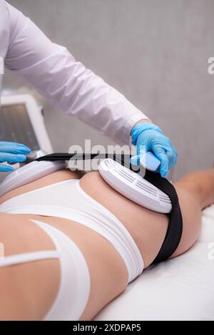 Professionelle Elektrostimulation-Sitzung, Nahaufnahme von Therapeutin, die EMS-Gerät auf Frau in der modernen Klinik anwendet, Muskeltonisierung, Körpermodellierung Stockfoto