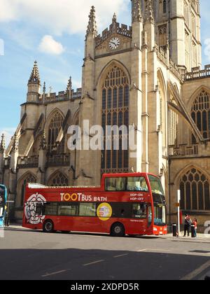 Toot Bus Hop-on-Hop-off-Bus mit geführter Stadtbesichtigung, in dem Personen in den Bus steigen und aus dem Bus steigen, und Bath Abbey im Hintergrund. Bath, Somerset, Großbritannien Stockfoto