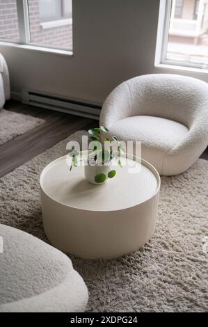 Modernes Wohnzimmer mit rundem, weißem Tisch, Pflanzen und gemütlichen Stühlen. Stockfoto