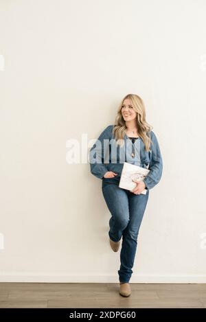 Lachende Frau, die sich an die Wand lehnt und einen Laptop hält Stockfoto