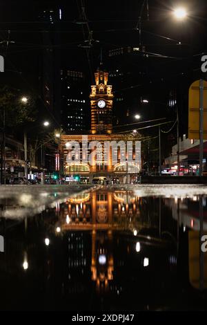 Die Flinders Street Station ist nachts beleuchtet und reflektiert in der Pfütze Stockfoto