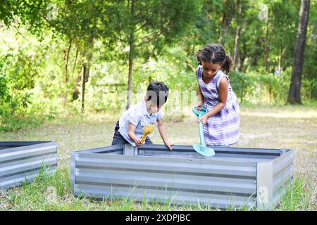 Zwei Kinder graben in erhöhten Gartenbeeten in einem bewaldeten Bereich. Stockfoto