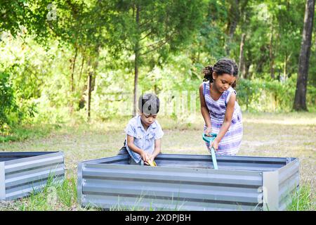 Zwei Kinder, die Schaufeln benutzen, um im Freien in Hochbeeten zu Garten zu gehen. Stockfoto