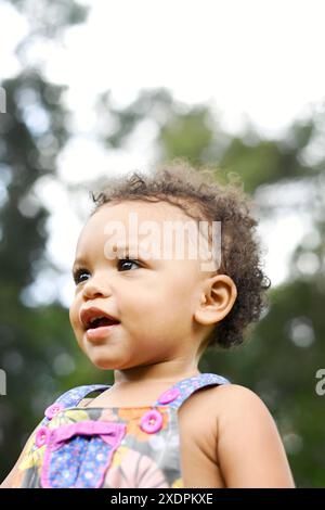 Nahaufnahme eines lächelnden Kleinkindes im farbenfrohen Outfit, draußen. Stockfoto