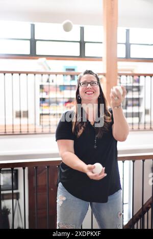 Frau jongliert glücklich mit weißen Bällen in einem hellen Innenraum. Stockfoto