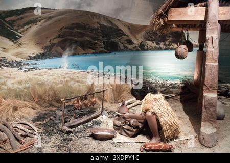 Ein Diorama des Maori-Lebens im Canterbury Museum, das einen Mann zeigt, der vor seiner Hütte Essen kocht. Körniges Bild, das bei verfügbarem Licht aufgenommen wird. Stockfoto