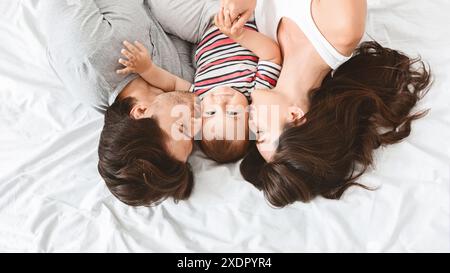 Glückliche Familie, die das Neugeborene im Bett küsst Stockfoto