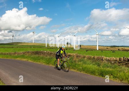 Radfahrer fahren auf einer Landstraße in South Yorkshire, an einem sonnigen Frühlingstag an einer Trockenmauer mit Windrädern und Wolken dahinter Stockfoto