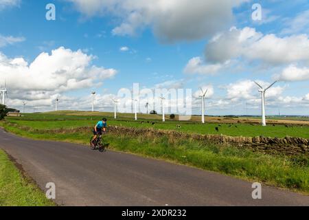 Radfahrer fahren auf einer Landstraße in South Yorkshire, an einem sonnigen Frühlingstag an einer Trockenmauer mit Windrädern und Wolken dahinter Stockfoto