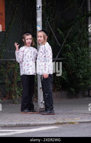 Früh an einem Sonntagmorgen warten zwei orthodoxe jüdische Jungen, fast sicher Brüder, auf einen Schulbus. In Williamsburg, Brooklyn, New York. Stockfoto