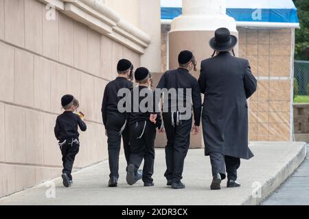 Ein Vater und seine 4 identisch gekleideten Söhne steigen einen Hang hinauf, um eine Synagogenfeier zu besuchen. In Kiryas Joel, Orange County, New York. Stockfoto