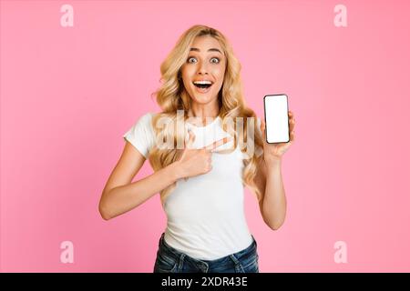 Staunende Frau, Die Smartphone Mit Leerem Bildschirm Auf Rosa Hintergrund Hält Stockfoto