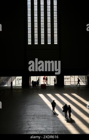 Die Menschen werden von der Nachmittagssonne umrahmt, während sie durch die Turbine Hall der Tate Modern Gallery laufen. Tate Modern, Bankside, London, Großbritannien. Stockfoto