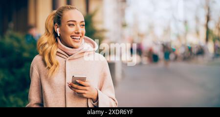 Glückliche Frau, die in der City Street mit Telefon und Ohrstöpseln läuft Stockfoto