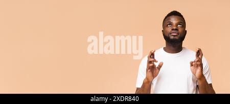 Mann, der die Finger überquert und nach oben blickt vor Peach Hintergrund Stockfoto