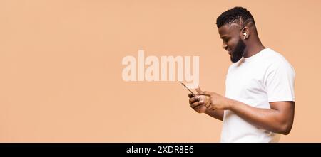 Mann, Der Das Smartphone Benutzt, Während Er Ohrstöpsel Vor Peach-Hintergrund Trägt Stockfoto