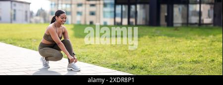 Fröhliche junge afroamerikanische Frau, die Schnürsenkel an ihren Turnschuhen bindet Stockfoto