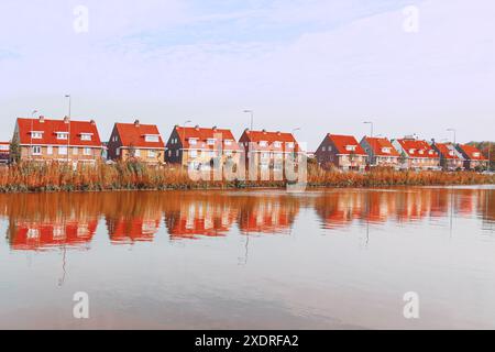 Eine Reihe von Häusern mit roten Dächern sitzt auf einem See. Die Häuser sind alle unterschiedlich groß und liegen entlang der Küste. Das Wasser ist ruhig und spiegelt die Ho wider Stockfoto