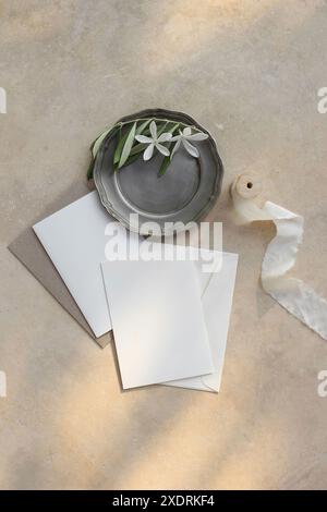 Sommer Hochzeit Schreibwaren. Geburtstagsmodelle. Leere Grußkarten, Einladungen auf Vintage-Teller mit weißen Blüten, Olivenzweige. Beige Marmor Stockfoto