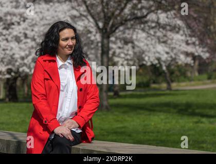 Romantisches Porträt einer stilvollen Frau in rotem Mantel und weißer Bluse. Positive Stimmung. Eine Dame läuft durch einen Stadtpark, sitzt auf der Attika und genießt einen Stockfoto