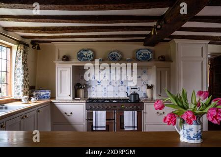 Rosafarbene Tulpen und Wasserkocher auf Herd mit Delfter Fliesen in Balkenküche des Tudor Farmhouse aus dem 16. Jahrhundert, Hertfordshire, England, Großbritannien Stockfoto