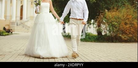 Brautpaar, Braut in weißem Kleid mit Blumenstrauß und Bräutigam im Hemd, der Hände hält, spaziert im Sommerpark Stockfoto