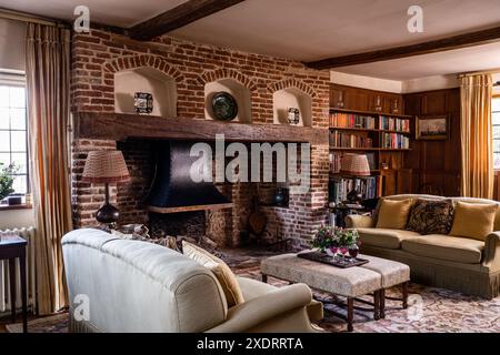 Ornamente auf dem Kaminmantel mit gemauertem Kamin mit Bücherregalen und Sofas im Tudor Farmhouse aus dem 16. Jahrhundert, Hertfordshire, England, Großbritannien. Stockfoto