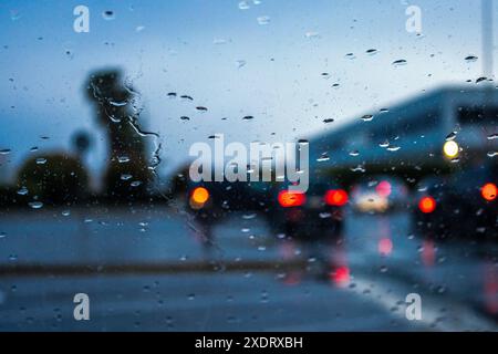 Durch Glassicht auf Fahrzeuge mit roten Rücklichtern, während Sie in der Regenzeit auf Asphaltstraße mit Gebäude überfallen Stockfoto