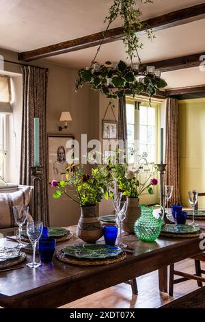 Kronleuchter mit Ifeu auf einem antiken Ulmentisch mit Schnittblumen und blauem Glas im charmanten Somerset-Pfarrhaus aus dem 17. Jahrhundert, Südwesten Stockfoto