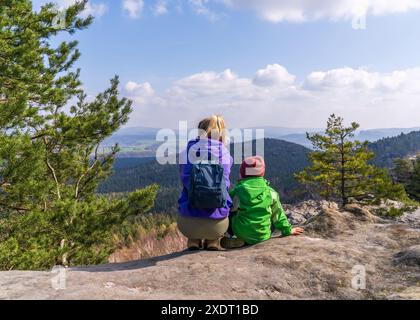 Eine junge Mutter und ihr kleiner Sohn sitzen auf einem Felsen und genießen die wunderschöne Berglandschaft. Rückansicht. Nationalpark Sächsische Schweiz in der Nähe Stockfoto