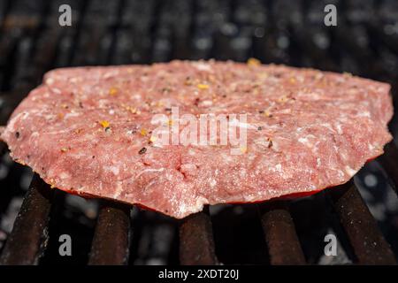 Ein hausgemachtes gefrorenes Burger-Patty wird auf einen Gasgrill gelegt und beginnt zu kochen. Stockfoto