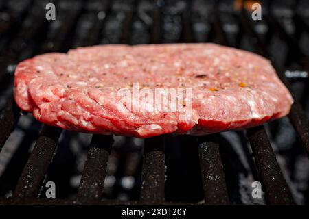 Ein hausgemachtes gefrorenes Burger-Patty wird auf einen Gasgrill gelegt und beginnt zu kochen. Stockfoto