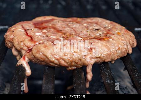 Ein hausgemachtes gefrorenes Burger-Patty wird auf einem Gasgrill platziert. Patty ist teilweise gekocht. Bereit für einen Flip. Stockfoto