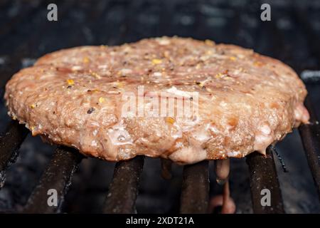 Ein hausgemachtes gefrorenes Burger-Patty wird auf einem Gasgrill platziert. Patty ist teilweise gekocht. Bereit für einen Flip. Stockfoto